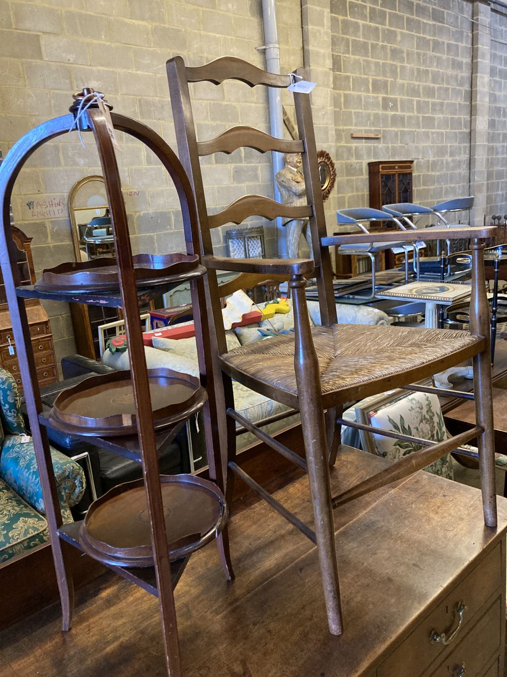 An Arts & Crafts ladder-back rush-seat elbow chair and an Edwardian inlaid mahogany three-tier cake stand (faults), 96cm high